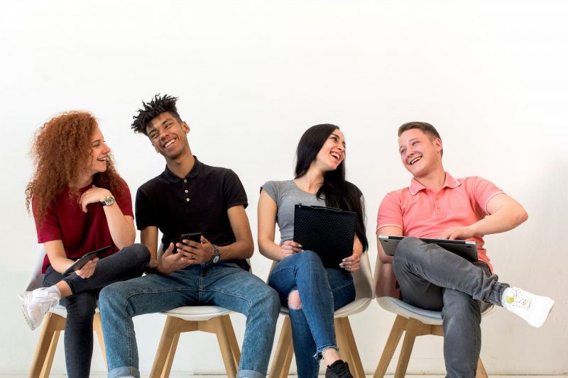 cheerful-multiethnic-friends-holding-electronic-gadget-sitting-classroom