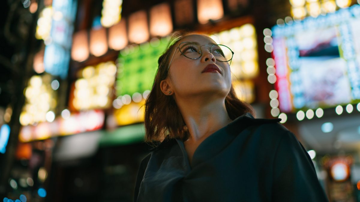 A portrait of young woman at night while looking up in the street.