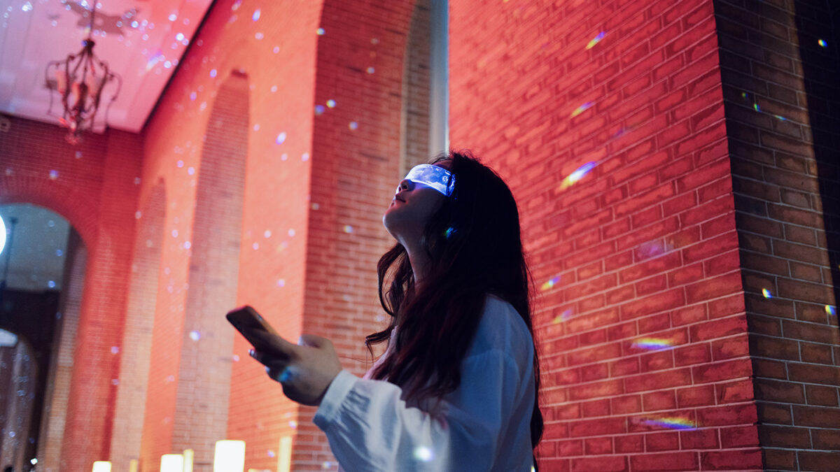 Woman wearing augmented reality glasses standing in night street using smartphone