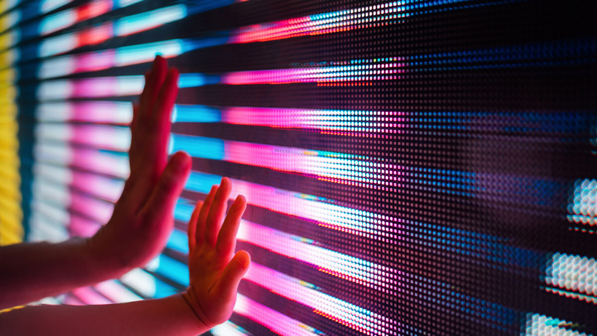 Close up of a mother and kid's hand touching illuminated and multi-coloured LED display screen, connecting to the future